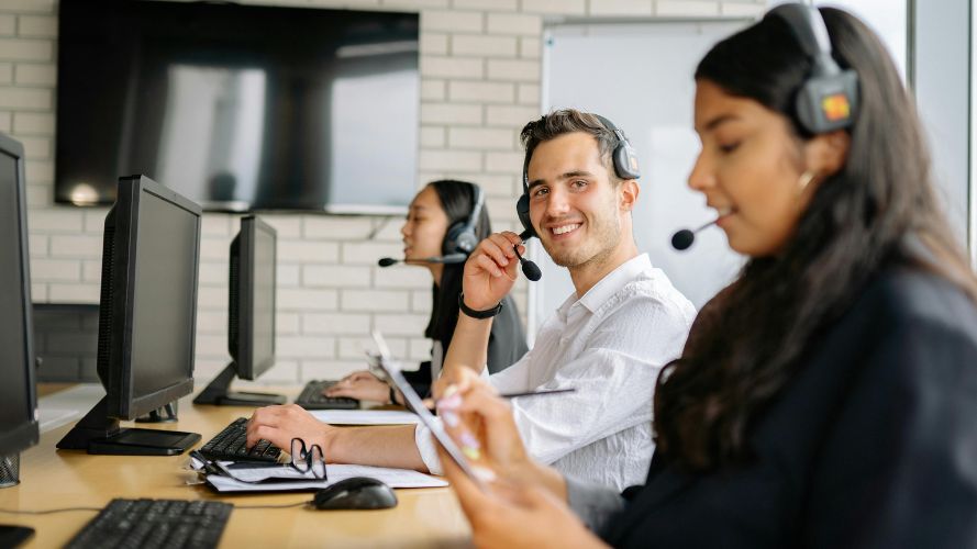 Three people on a training team are taking calls, smiling and working on their computers